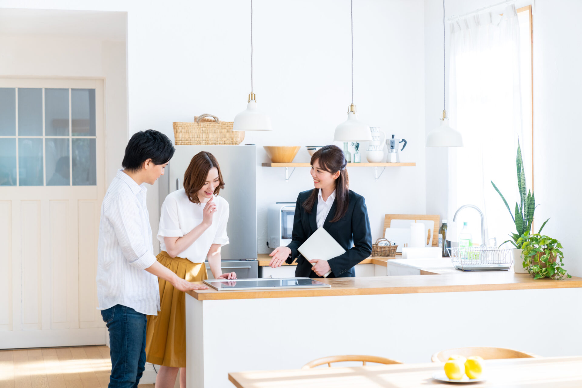 注文住宅のキッチン設備を説明する営業担当者と、相談するカップル。明るいナチュラルテイストのキッチン空間