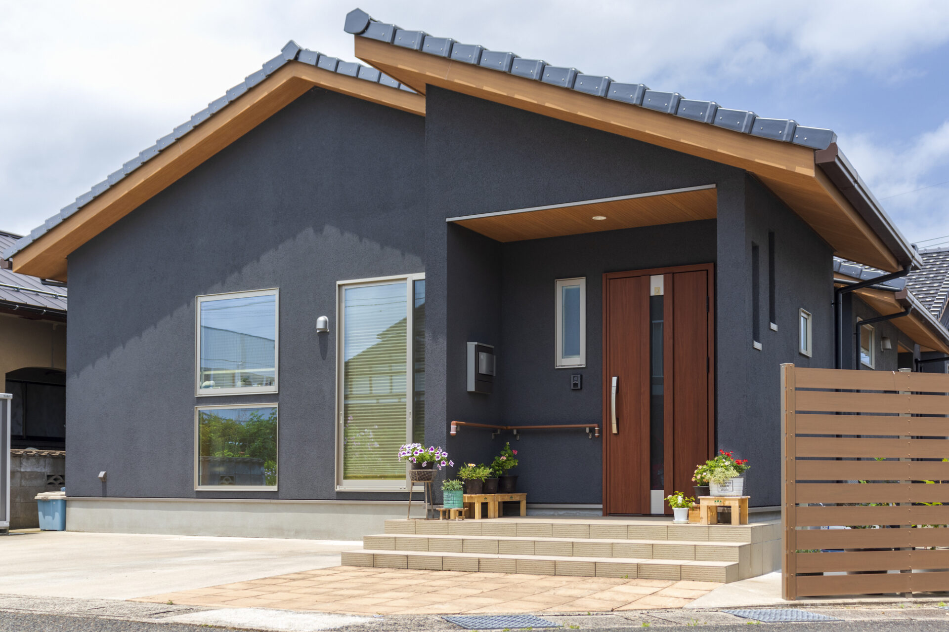 黒い外壁と木目調玄関ドアが特徴の平屋住宅外観｜段差の少ない玄関アプローチと花のある門まわり