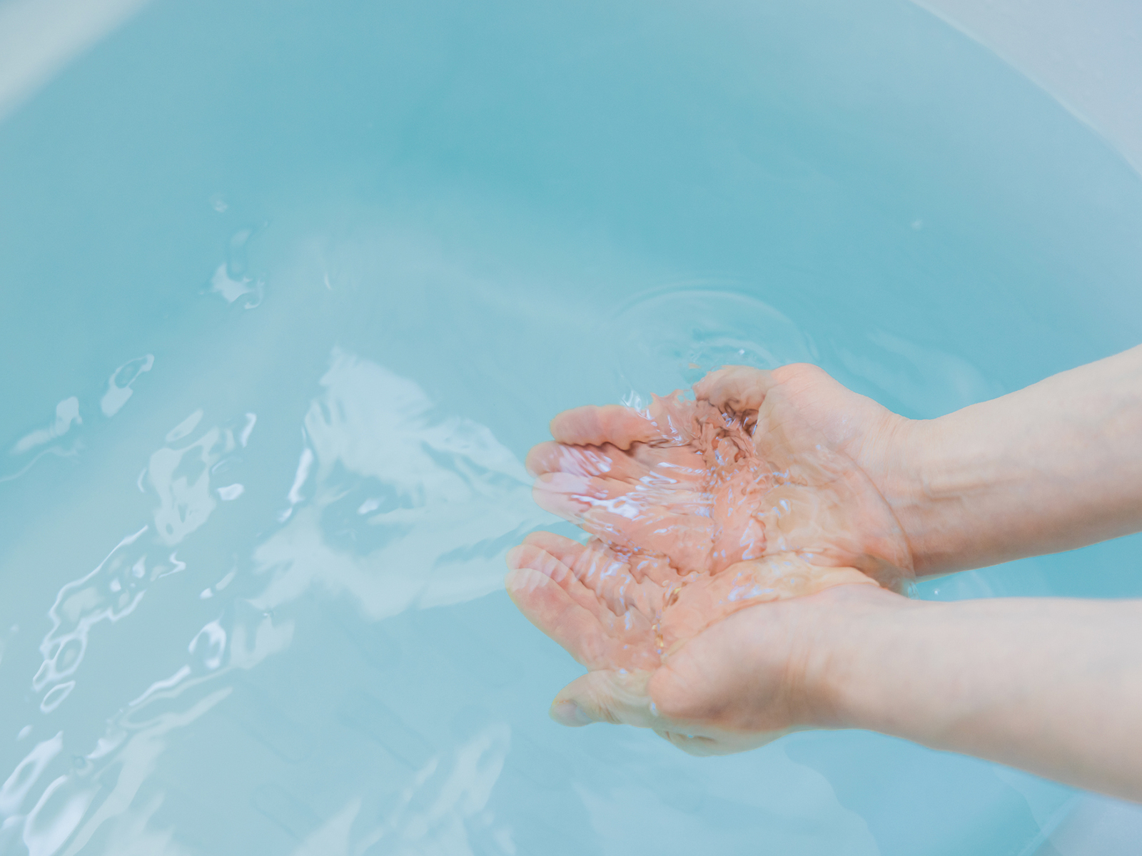 浴槽と水面、手で水を掬っている手の画像
